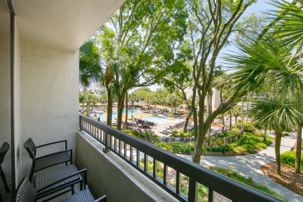 Balcony overlooking pool area and tall trees.