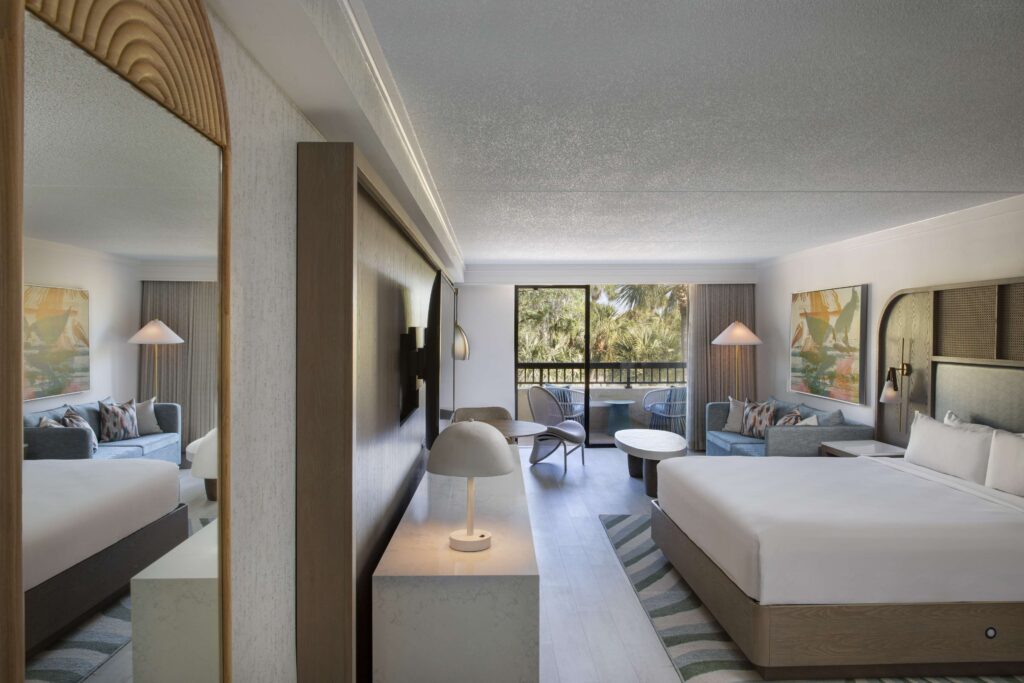 Large room with two beds, seating, and a balcony with lush greenery.