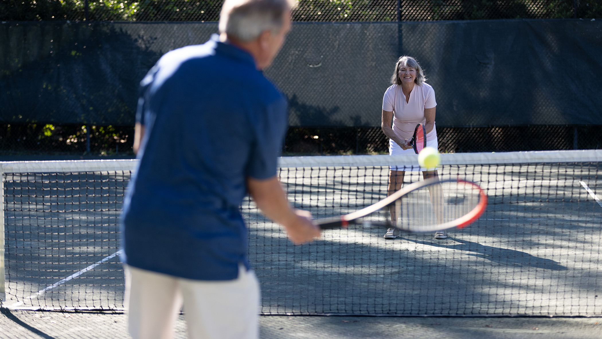 Older couple playing tennis on an outdoor court.