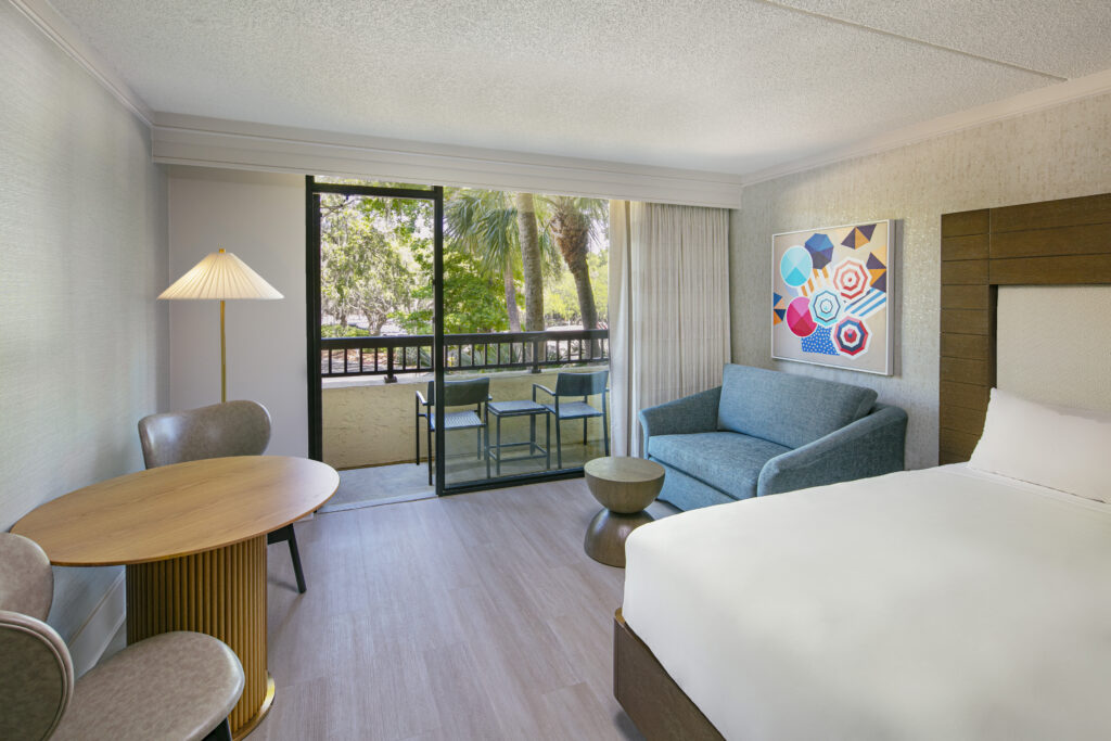 Bright hotel room with balcony and seating.