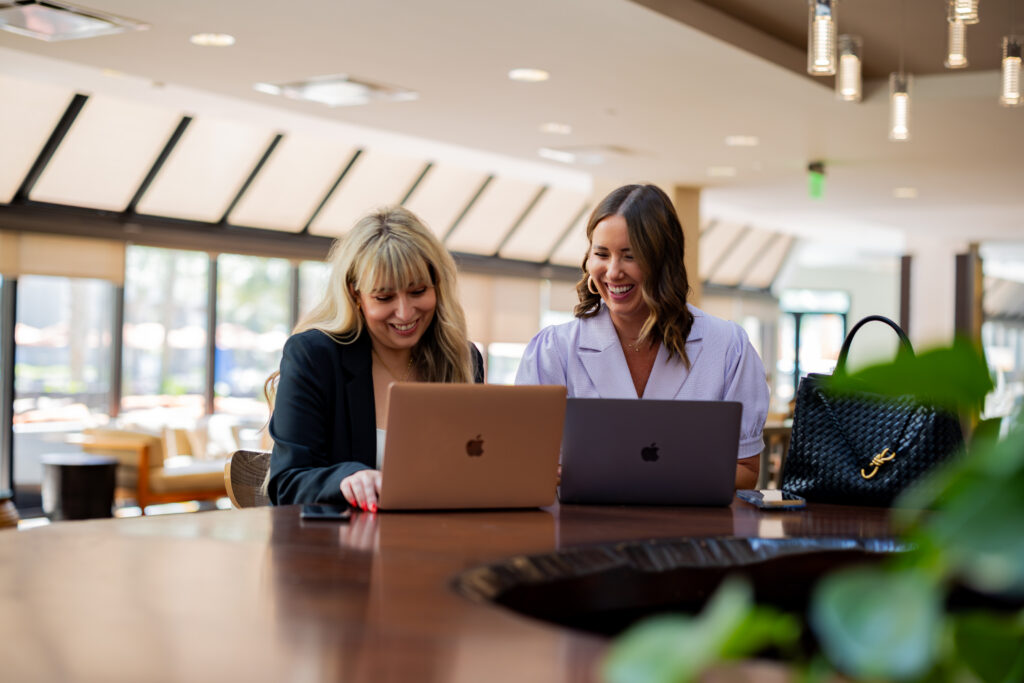 Two women smiling and working on laptops.