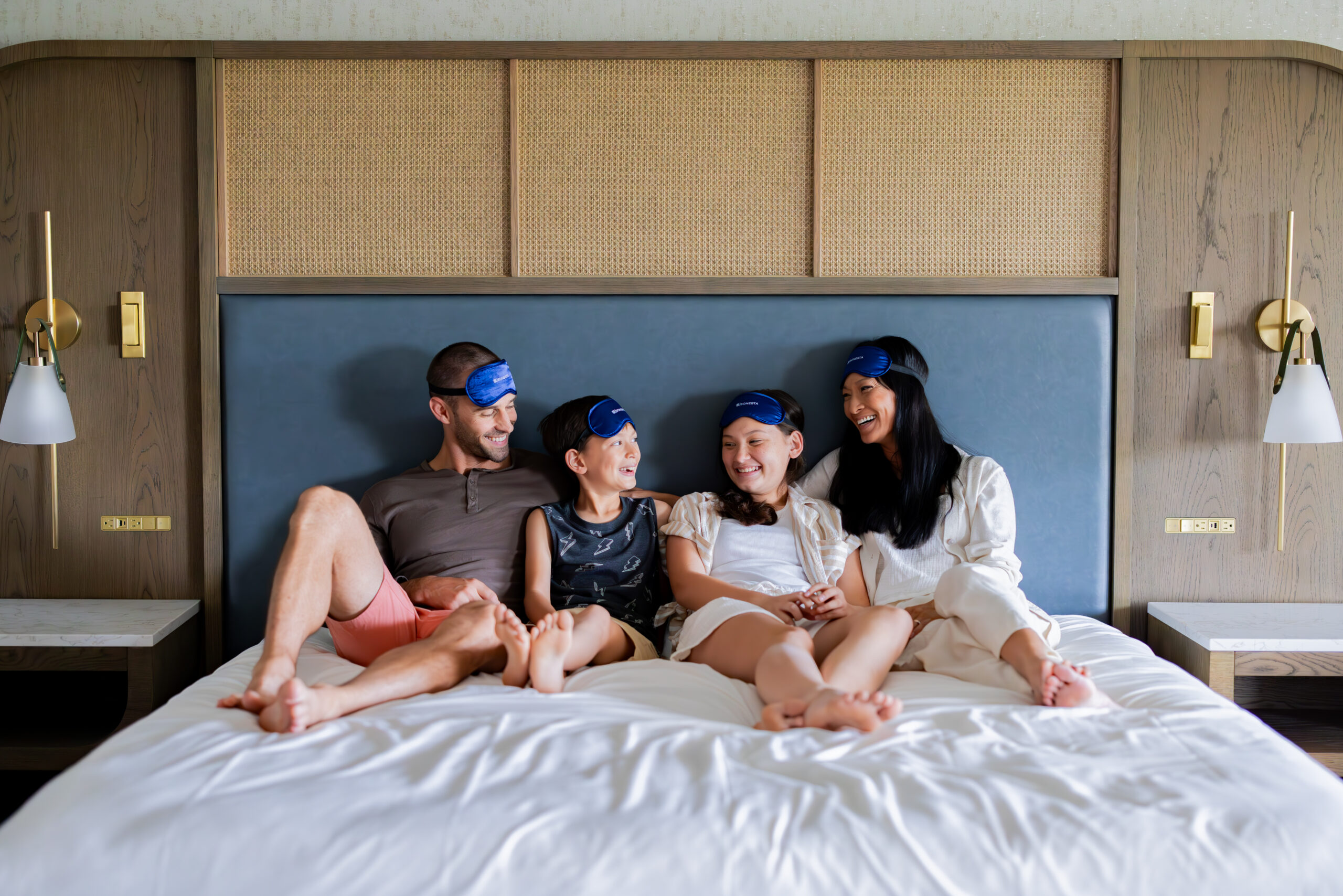 Family laughing in bed wearing sleep masks.