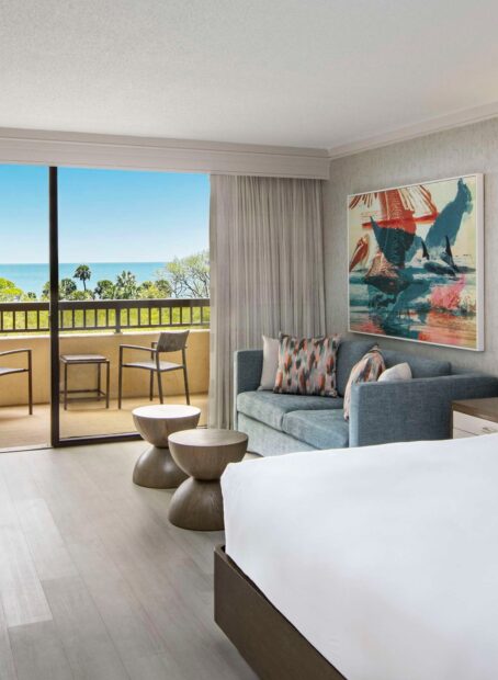 Hotel suite with balcony overlooking ocean and artwork.