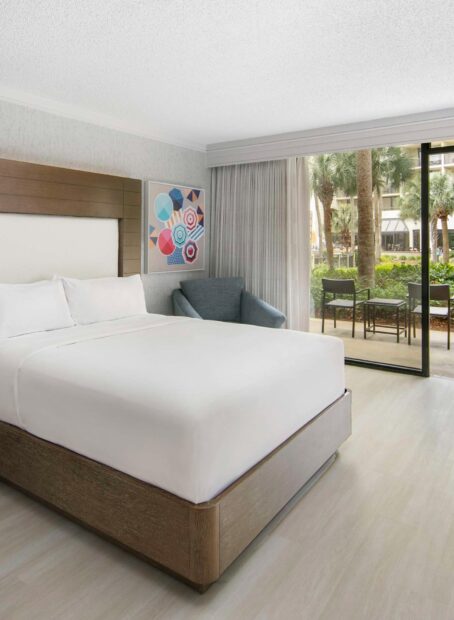 Bright hotel room with queen bed and balcony.